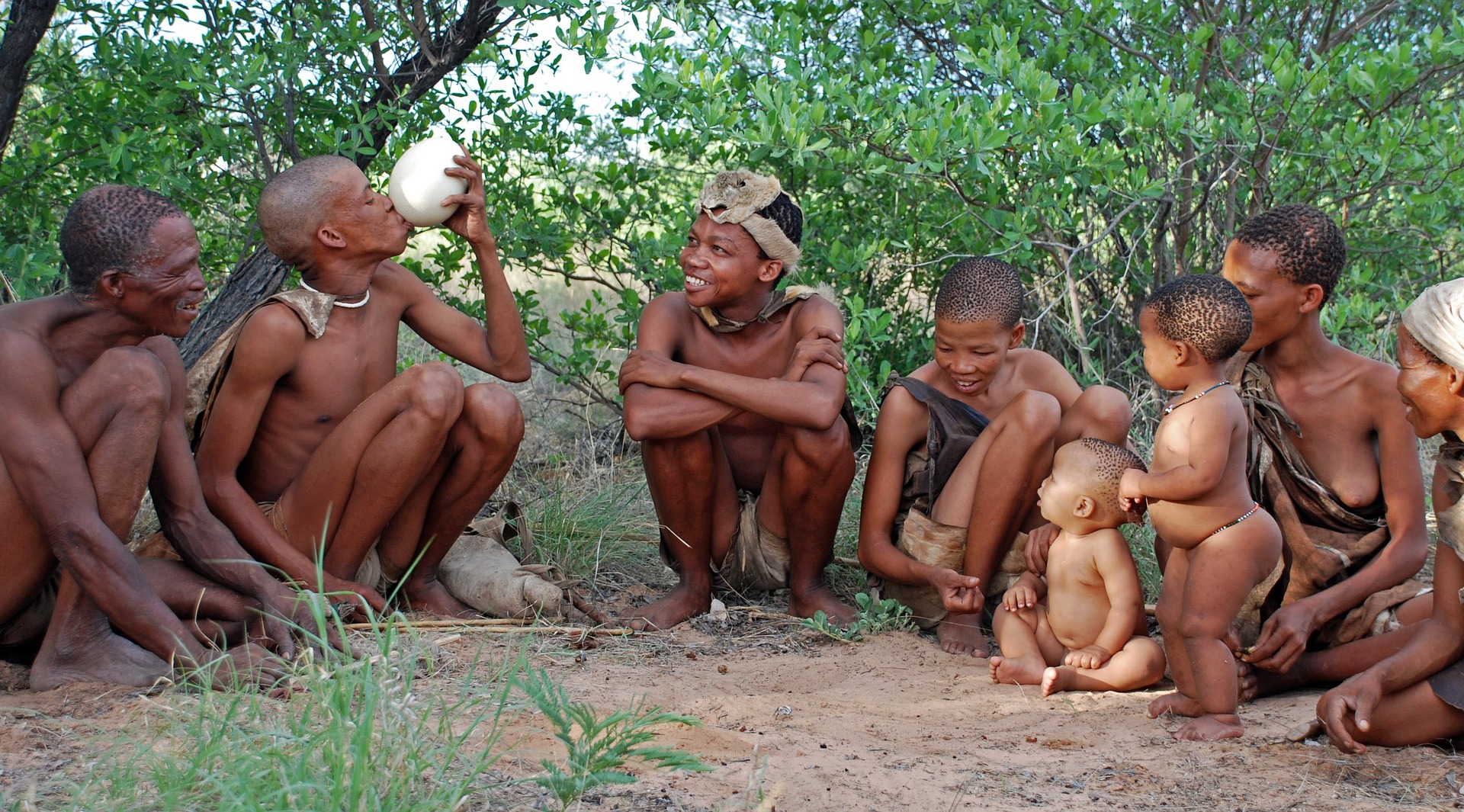 A group of San from southern Africa. They are happily squatting on the ground, exchanging smiles and joy. They are of all ages, from old, to baby.