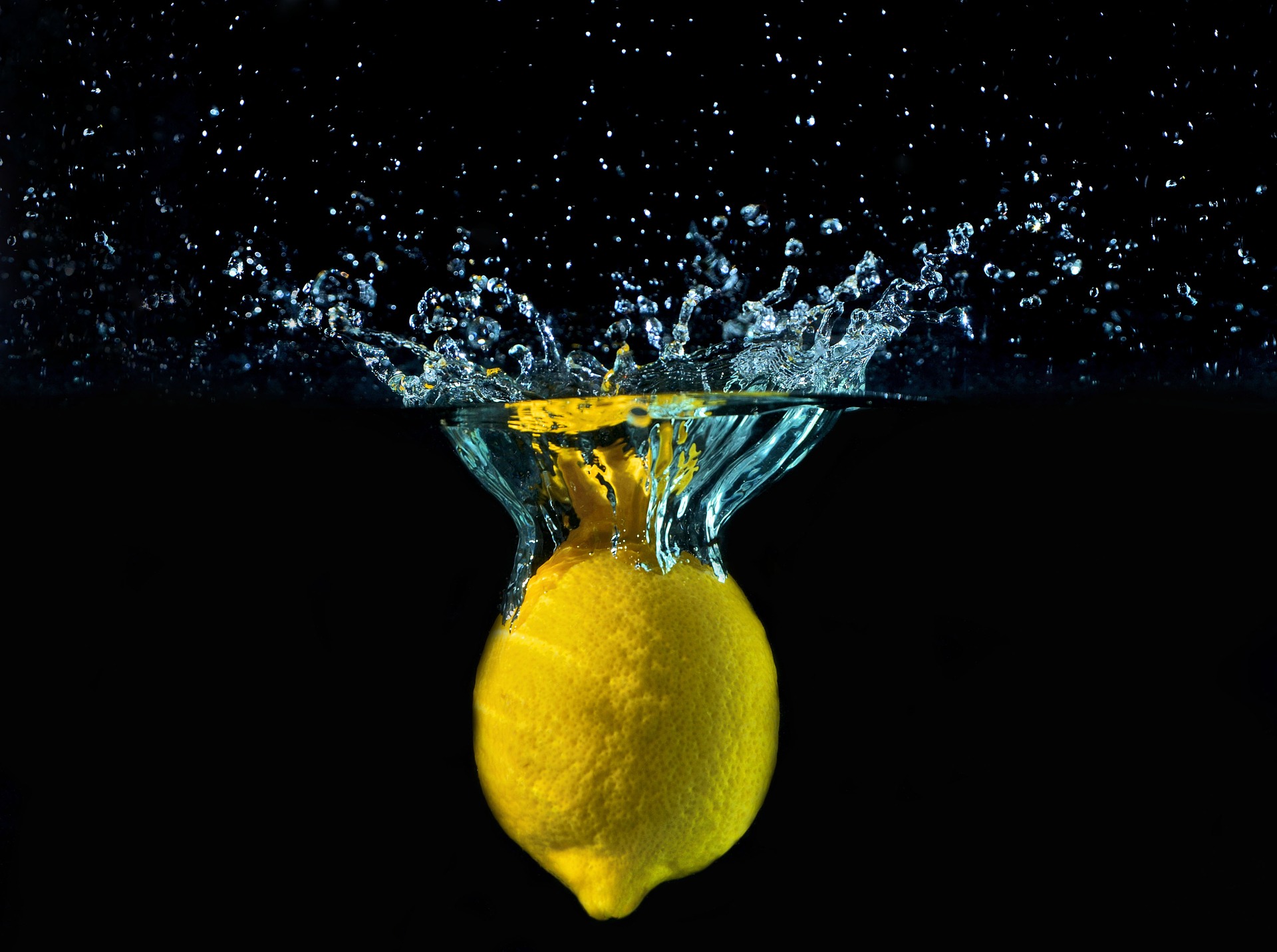 A bright yellow lemon lands in water; the background is black
