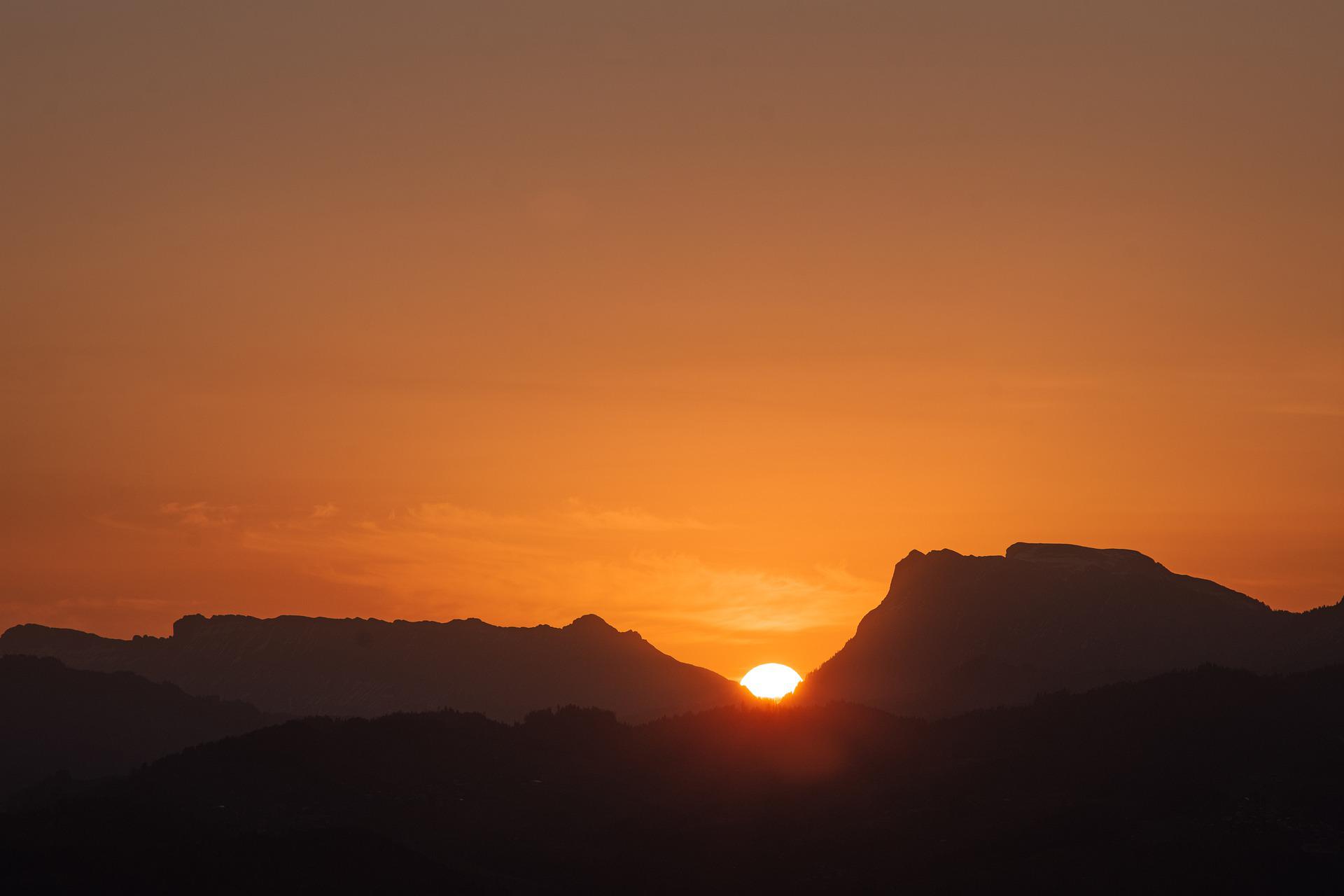On a darkened plains landscape, the sun is rising in a gap between two table mountains
