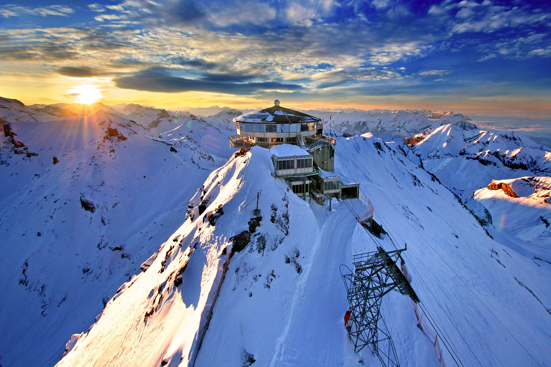 The sun is rising over the snowy mountain peaks of Switzerland. We see the mountain station atop Schilthorn, 2970 metres or 9740 feet.