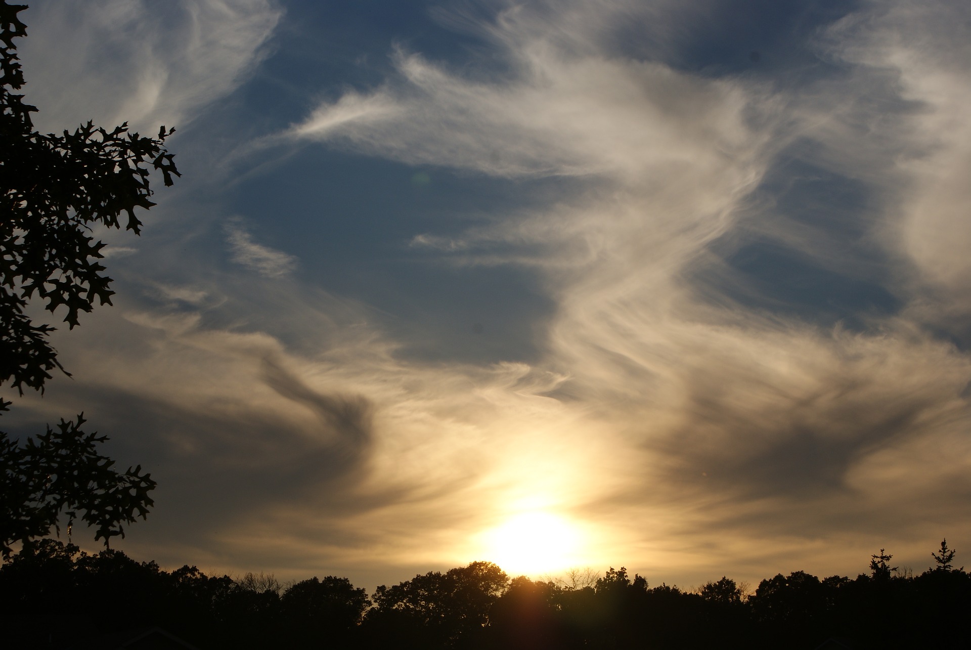 From a low-down darkened perspective, perhaps in a forest clearing, we see the sun low on the horizon, clouds in an angelic formation around