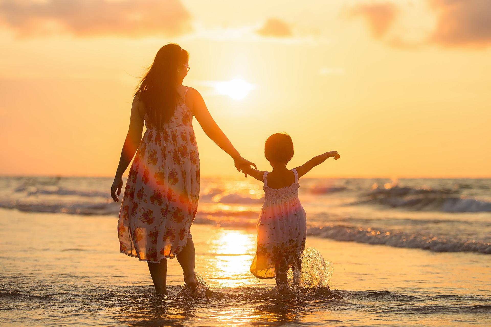 A mother and young daughter happily walk in the surf of a beach in the early morning sun