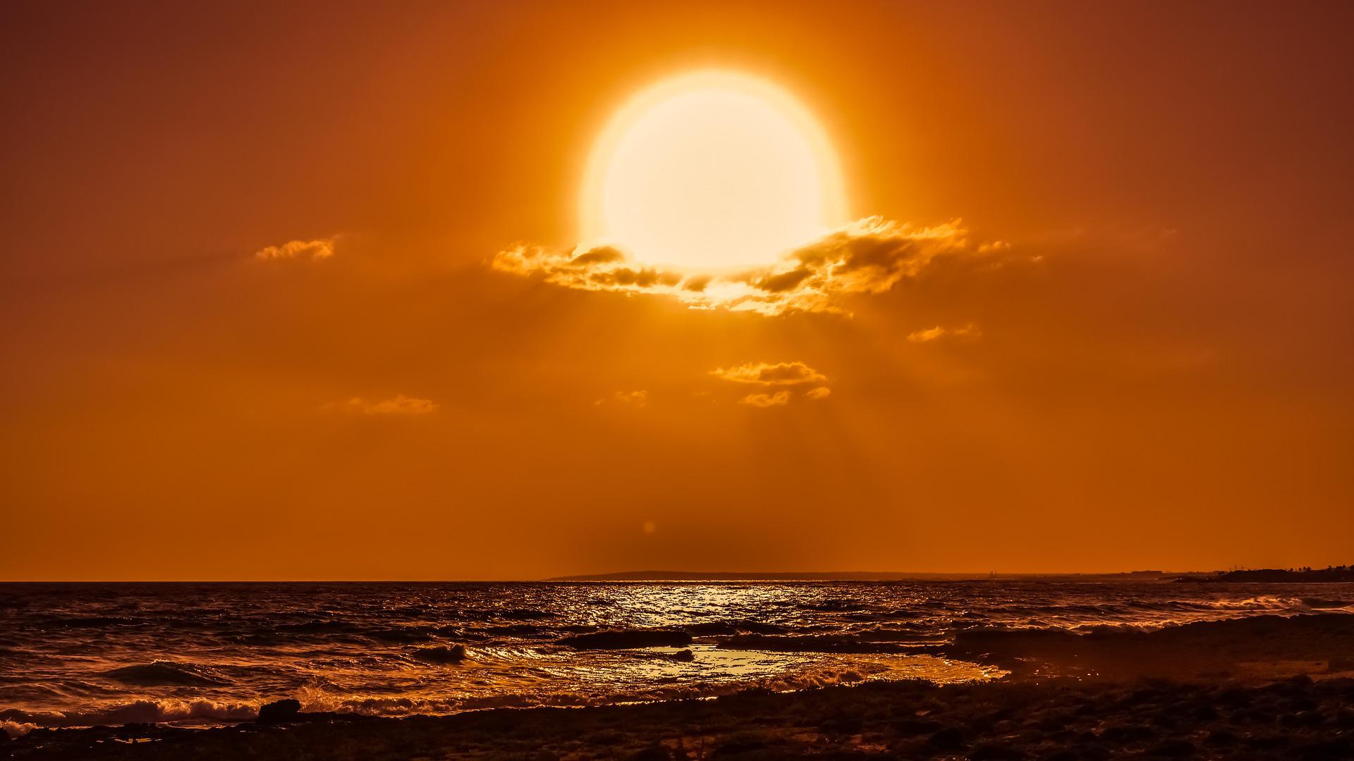 The huge golden sun is low on the ocean horizon. It looks as if clouds are being cleared from its face to reveal its glory. There even is a sense of the face of the sun detaching.