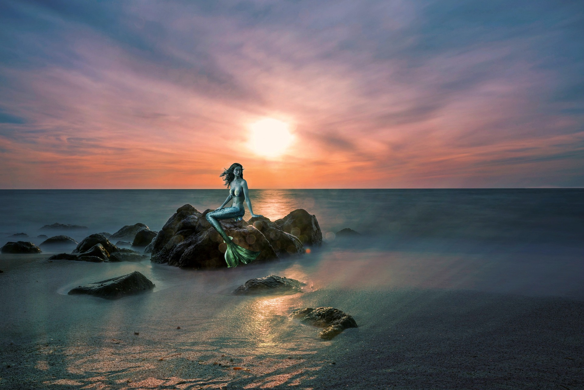 The sun is rising or setting. Where the sea meets the beach are some rocks. On one of these rocks sits a beautiful mermaid.