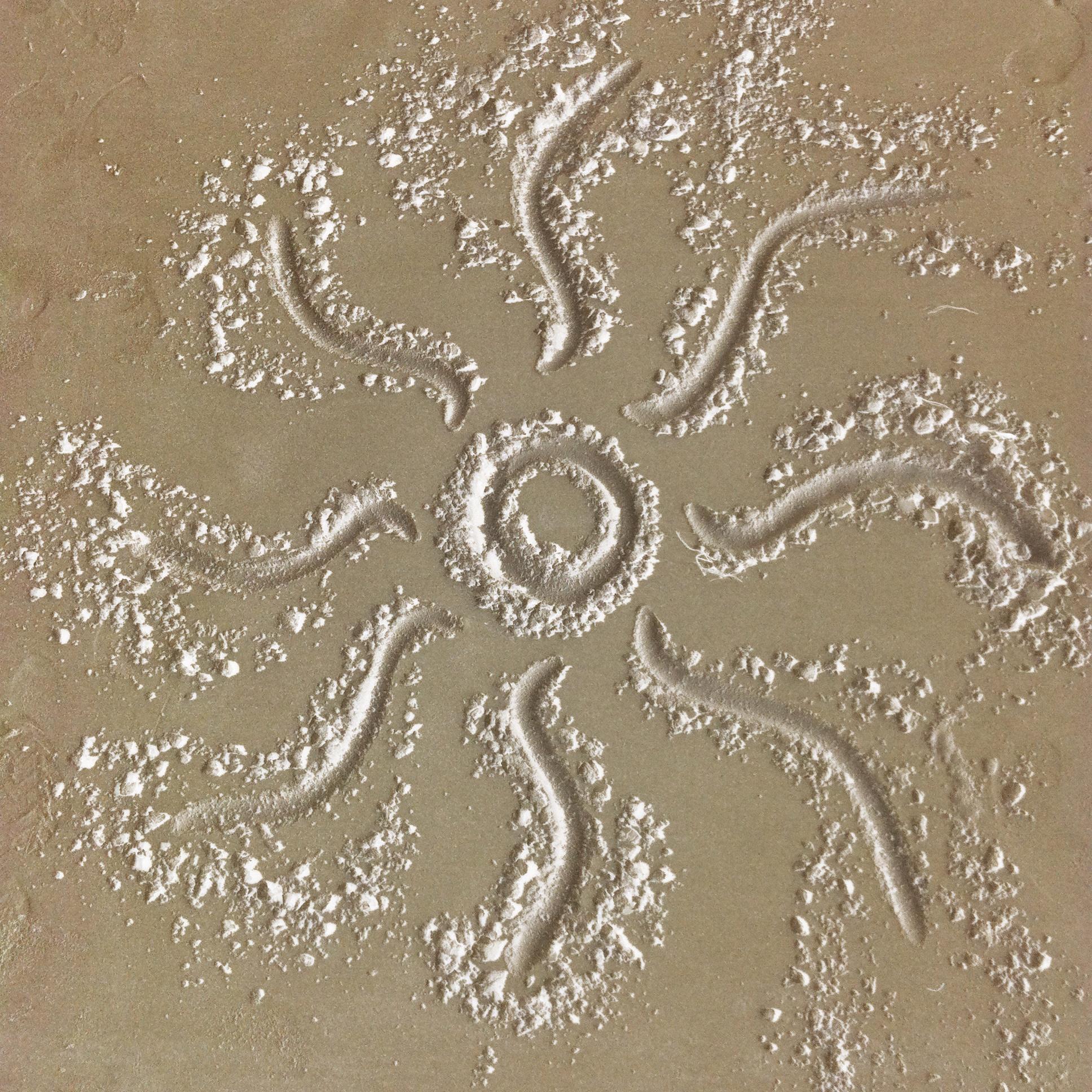 Into wet beach sand has been etched a sun with wavy rays. It is like a mandala, harmonious and perfect.
