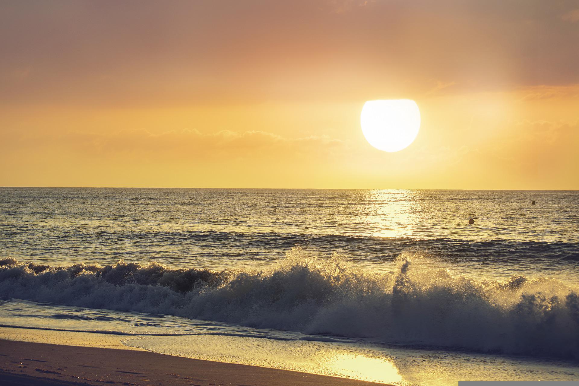 Viewing from a beach and its quiet surf, we see the rising sun has just lifted above the sea's horizon. The sun is bright and glorious, sacred and precious.