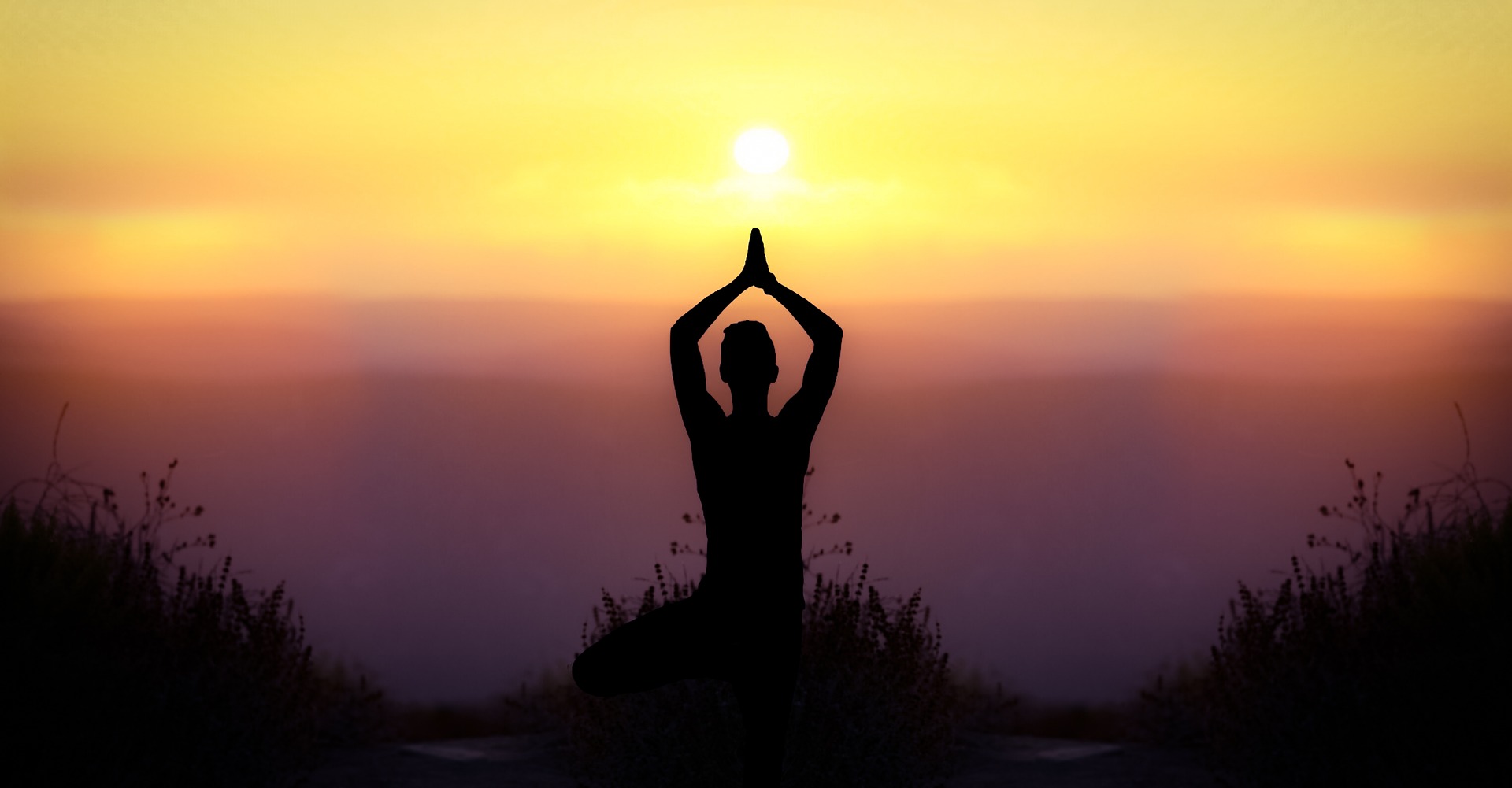 The silhouette of a human at sunrise or sunset, facing the sun, arms are extended above the head in a sacred way