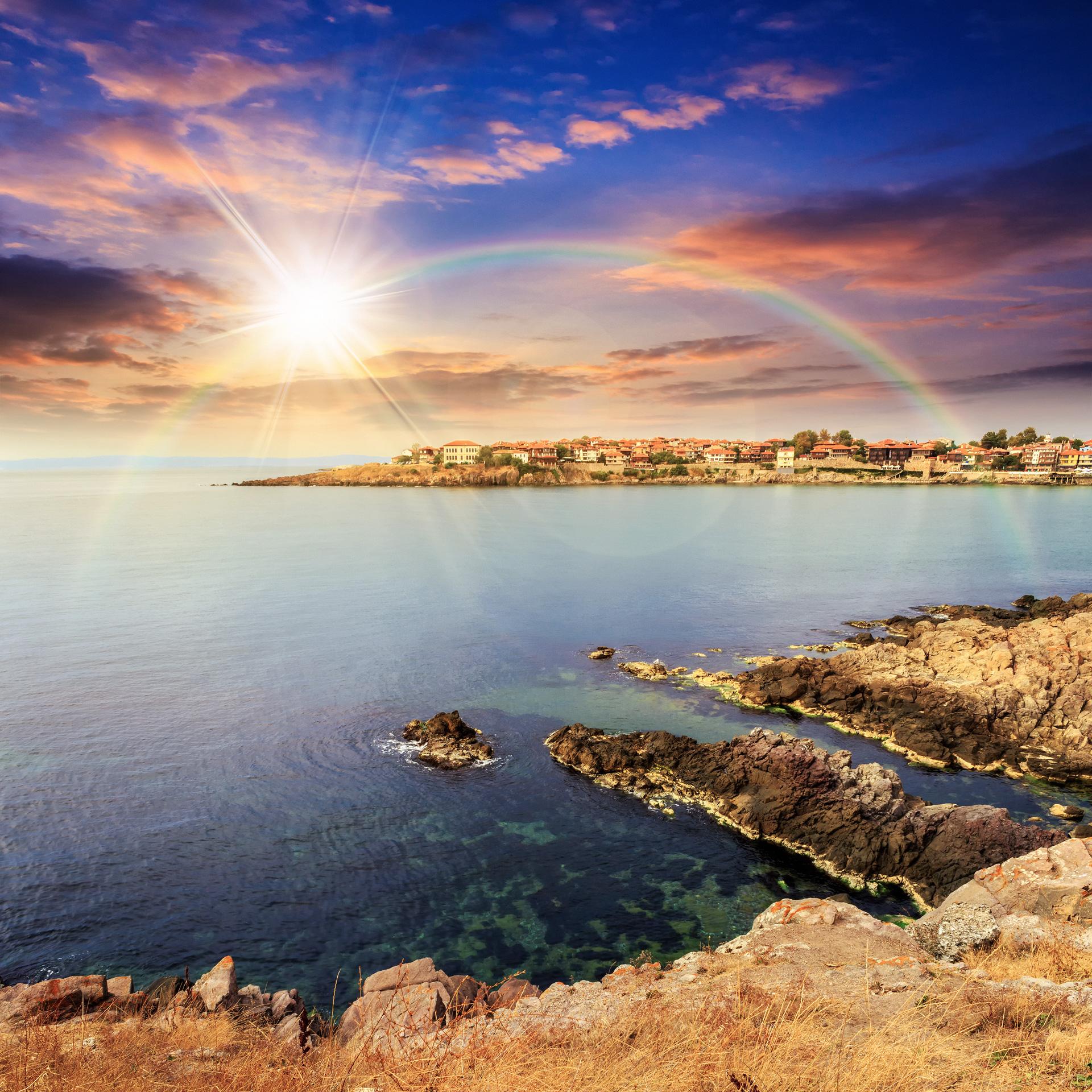 Maybe we have walked from the peninsula town and are now atop this cliff. We look out over the sea and see the rising sun, a deep blue sky, and an amazing rainbow arcing over the town.