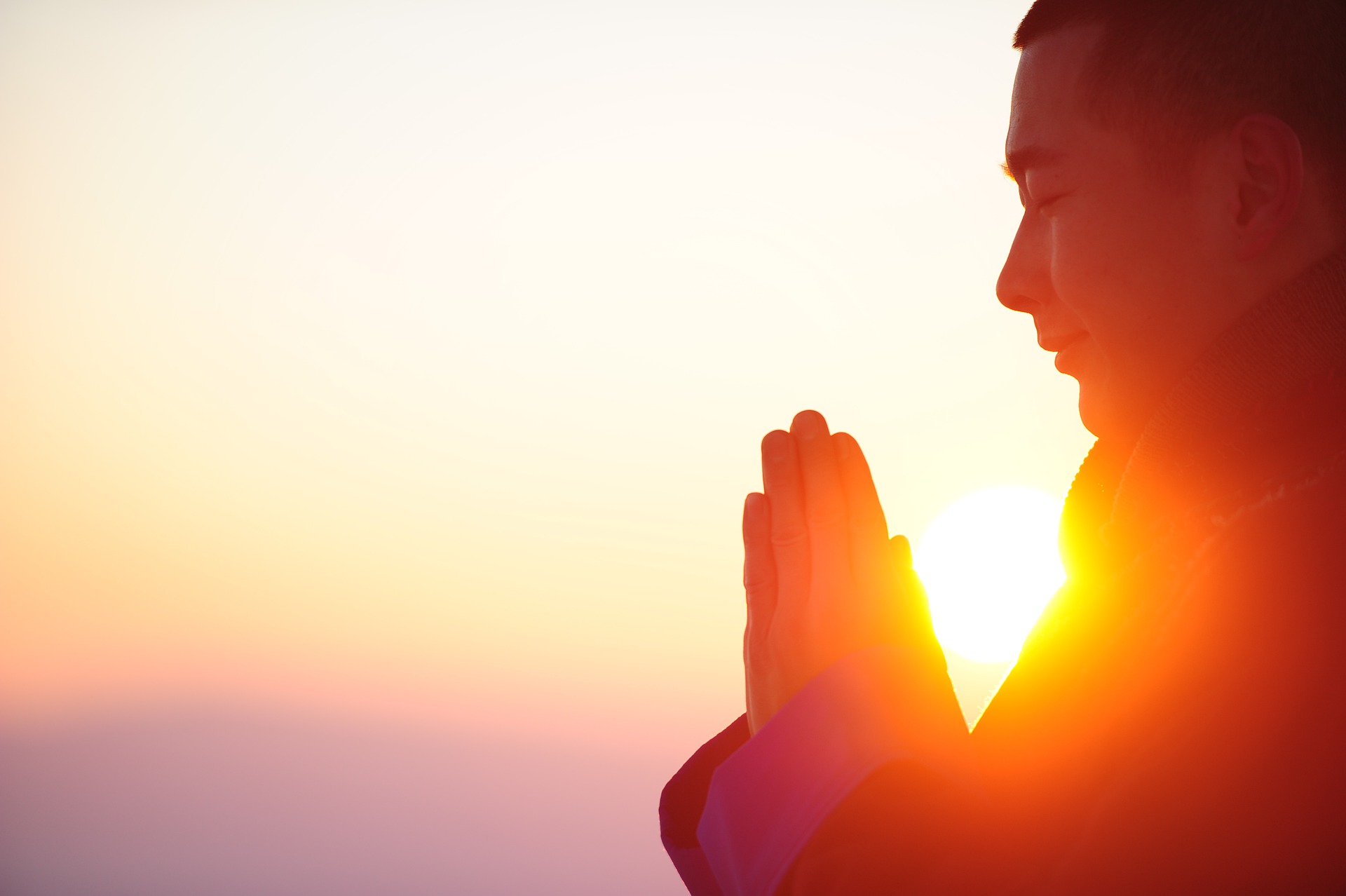 An oriental man, perhaps a Buddhist monk, is praying at the sunrise. We see,  on the right of the picture, part of his profile: his hands, part of his chest, and his head. The sun appears between his head and praying hands.