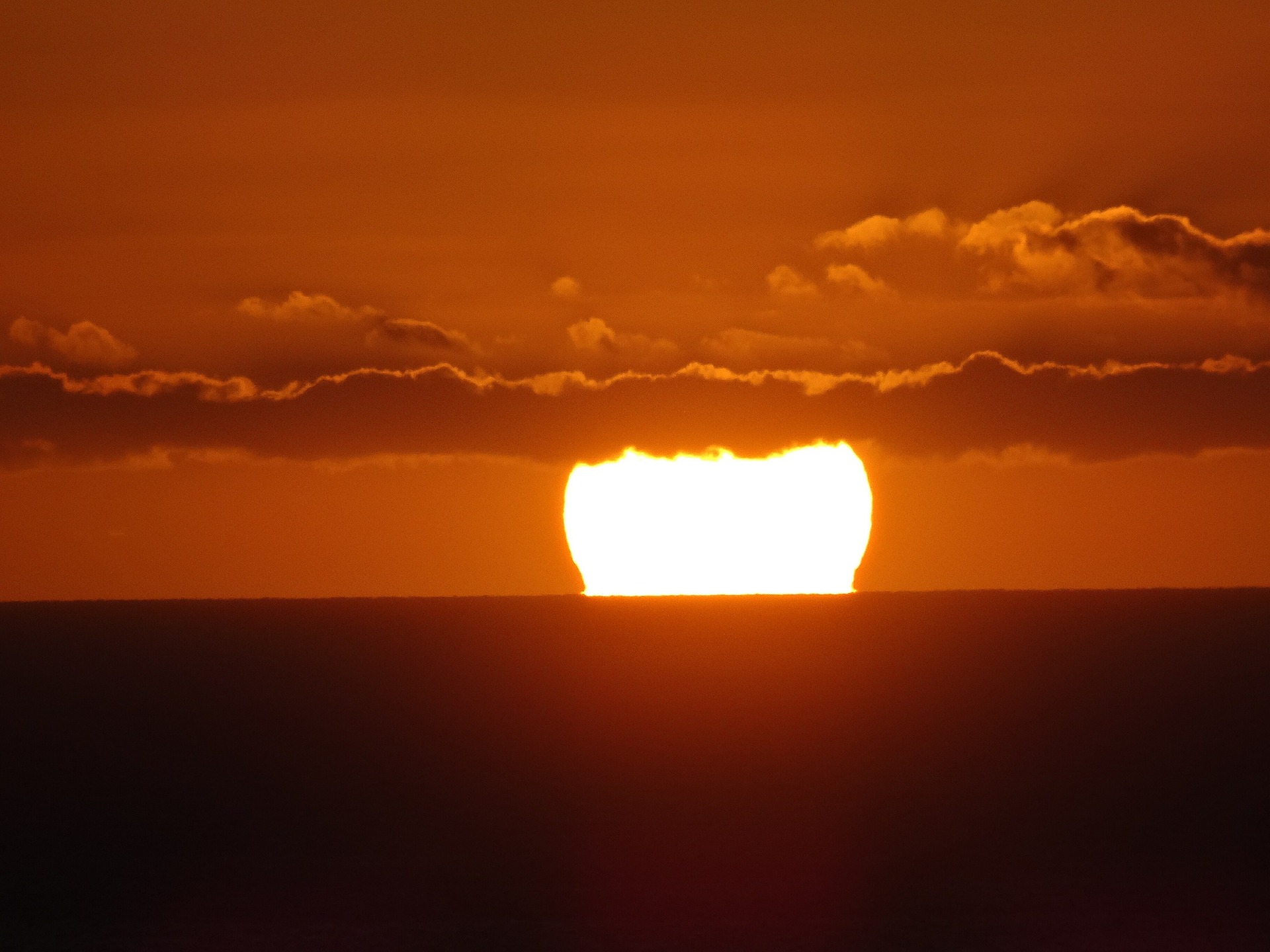 A big sun is rising or setting over the sea. There are a few low-lying wispy clouds.