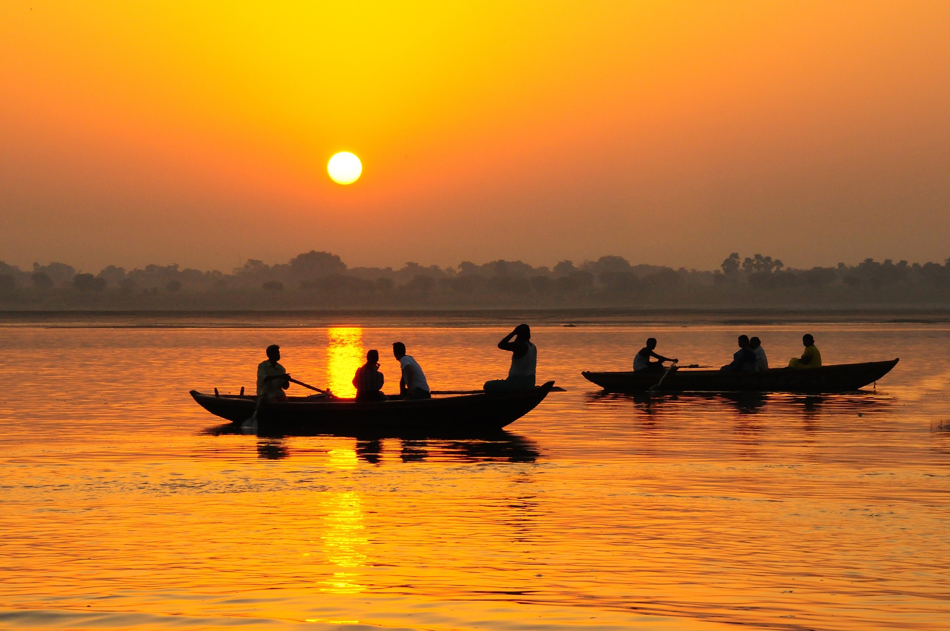 A sunrise over the River Ganges in India. Two small boats with men are in the foreground.