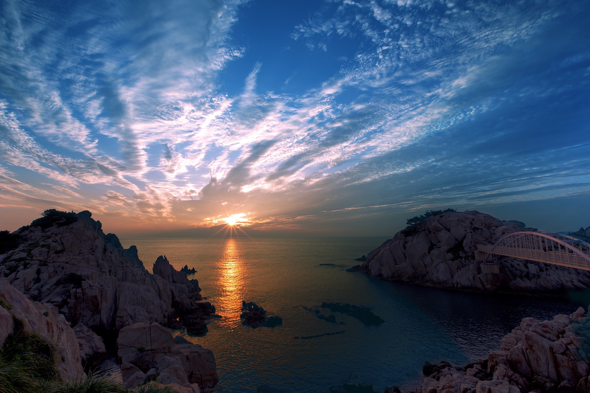 A sunrise in South Korea by the sea. There is a spectacular sky. A bridge is visible.