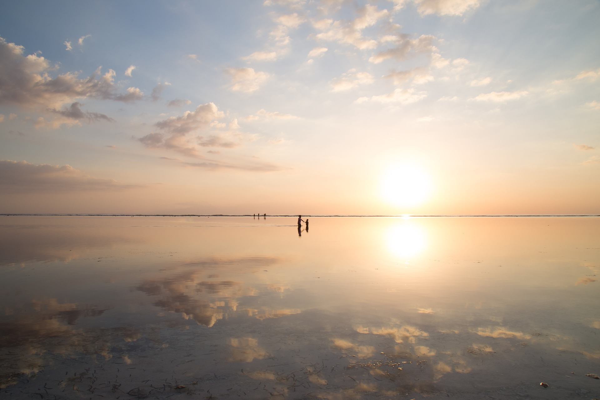 A sunrise somewhere in the world. A huge wet beach with a few people on it.