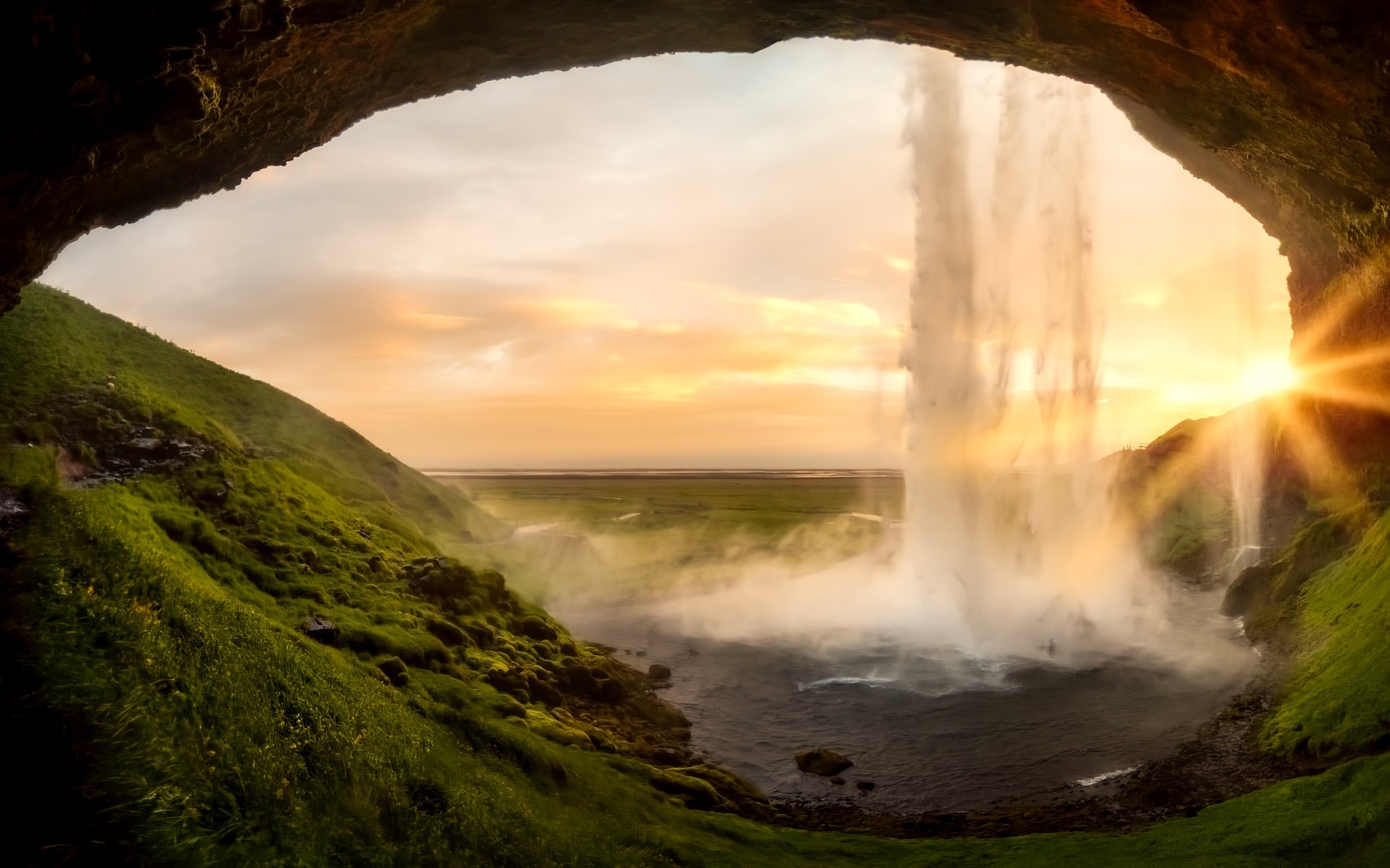 Sunrise at Iceland’s Seljalandsfoss Waterfall. We look out from the darkness behind the waterfall through a giant eye-shaped opening.