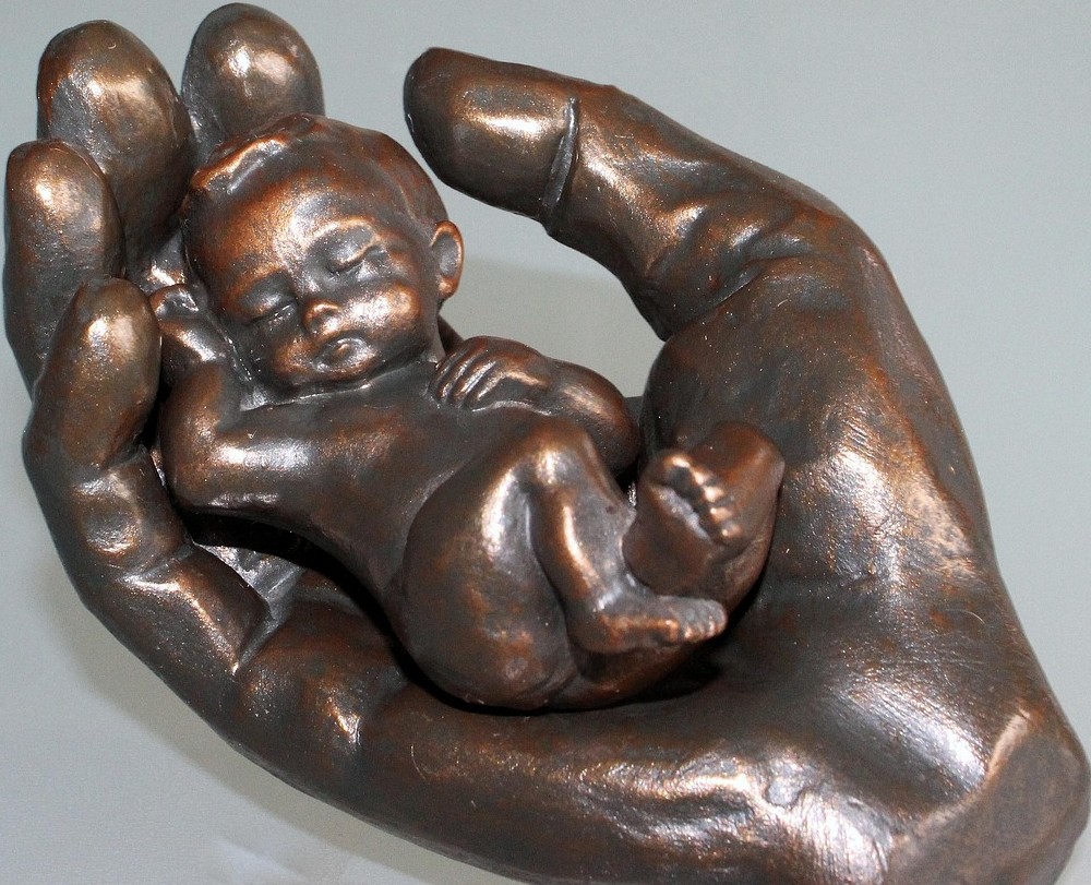 A bronze sculpture of a sleeping baby in a hand