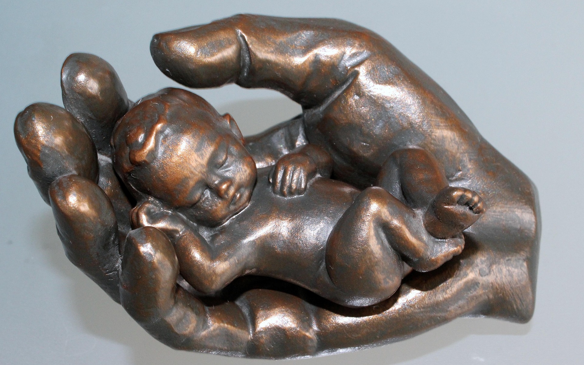 A bronze sculpture of a sleeping baby in protective hands