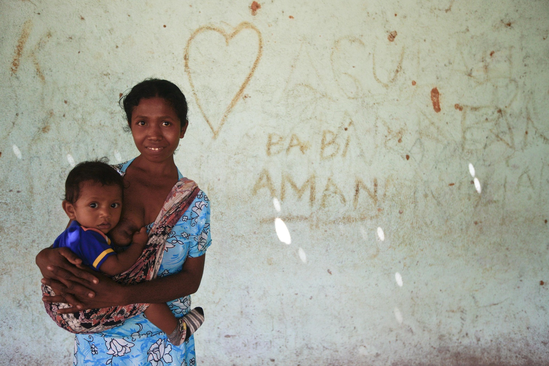 Smiling mother breastfeeding her slung child by a wall