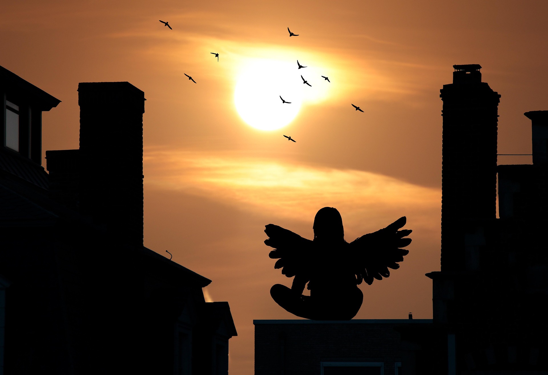 The silhouette of a seated angel on a roof gazing at the rising or setting Sun